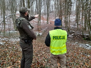 w lesie strażnik leśny wskazuje ręką policjantowi grodzisko wyżynne