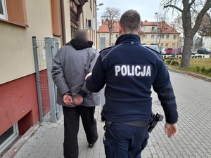 dzielnicowy prowadzi do komendy policji mężczyznę skutego kajdankami