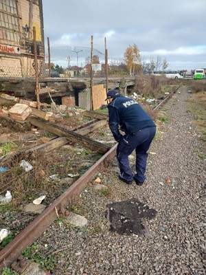 przy starej wyładowni PKP umundurowany policjant, pochyla się i spogląda pod rampę