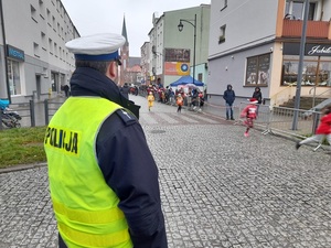 na skrzyżowaniu stoi policjant ruchu drogowego. Ulicą biegną dzieci