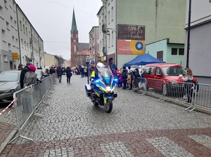 Przed dziećmi zebranymi na linii startu jedzie na motocyklu policjant ruchu drogowego