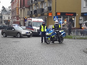 na skrzyżowaniu przed nieoznakowanym radiowozem i karetką znajdują się dwaj policjanci ruchu drogowego. Jeden z nich stoi przy policyjnym motocyklu