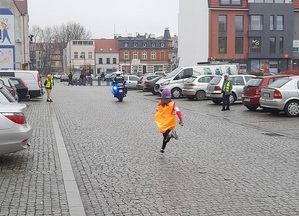 ulicą biegnie dziewczynka. Przed nią jedzie motocyklem policjant ruchu drogowego