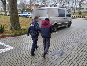 umundurowany policjant prowadzi zatrzymanego mężczyznę w kierunku nieoznakowanego radiowozu