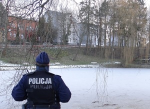 przed zamarzniętym stawem stoi umundurowany policjant