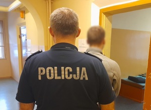 w otwartych drzwiach policyjnej celi stoi mężczyzna. Za nim stoi policjant służby dyżurnej