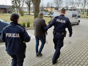 policjant prowadzi w stronę nieoznakowanego radiowozu mężczyznę. Za nimi idzie policjantka