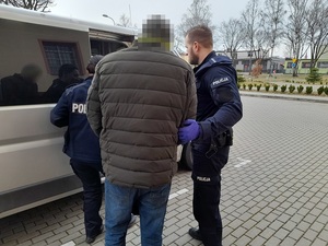 policjant i policjantka wprowadzają do nieoznakowanego radiowozu mężczyznę