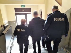 dwoje policjantów prowadzi mężczyznę schodami w dół w kierunku wyjścia z budynku komendy