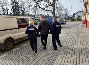 dwoje policjantów i zatrzymany mężczyzna przed nieoznakowanym radiowozem służby konwojowej