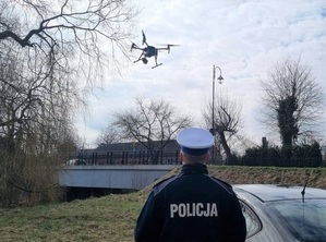 przy radiowozie stoi policjant ruchu drogowego. Nad nim leci dron