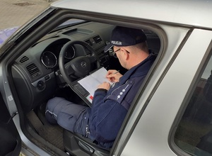 siedzący w radiowozie policjant wypisuje dokumentację