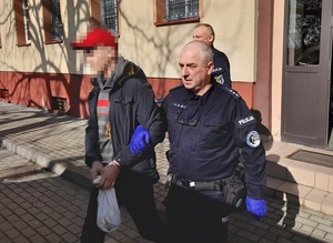 policjant wyprowadza z budynku komendy mężczyznę z rękoma skutymi kajdankami