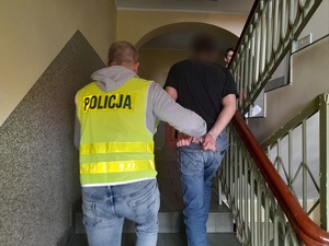 policjant prowadzi schodami mężczyznę skutego kajdankami