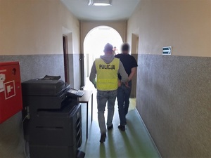 policjant prowadzi korytarzem skutego kajdankami mężczyznę