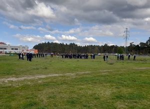 na obszarze zieleni przy placu zabaw i przed stadionem policjanci w strojach ochronnych używanych przy zabezpieczaniu imprez masowych otaczają grupę kibiców