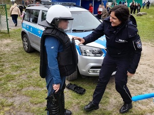 na festynie przy oznakowanym radiowozie policjantka uśmiecha się do chłopca ubranego w policyjny sprzęt ochronny