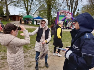 na festynie uśmiechnięta policjantka przygląda się dziewczynce przymierzającej narkogogle