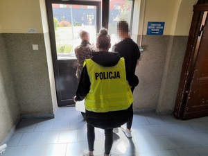 policjant i policjantka wyprowadzają z budynku komendy zatrzymanego mężczyznę