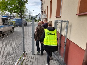 policjant i policjantka prowadzą zatrzymanego mężczyznę w kierunku radiowozu