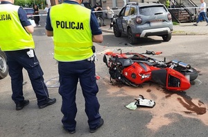 na skrzyżowaniu ulic leży uszkodzony motocykl. Przed nim znajduje się dacia duster. Przy motocyklu stoją dwaj policjanci ruchu drogowego