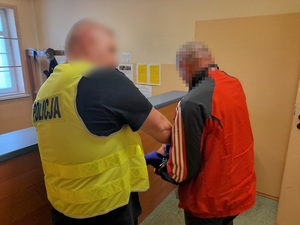 policjant w kamizelce odblaskowej zakłada kajdanki zatrzymanemu mężczyźnie