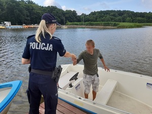 na jeziorem policjantka wręcza ulotkę mężczyźnie stojącemu w łodzi