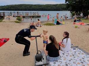 nad jeziorem na plażypolicjantka wręcza ulotkę dziecku