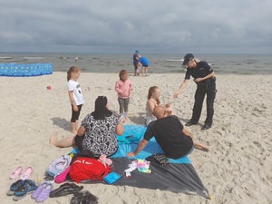 na plaży nad morzem policjantka wręcza ulotkę dziewczynie siedzącej na piasku