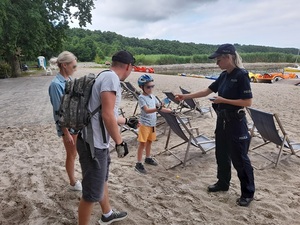 nad jeziorem policjantka wręcza ulotkę chłopcu będącego w towarzystwie rodziców