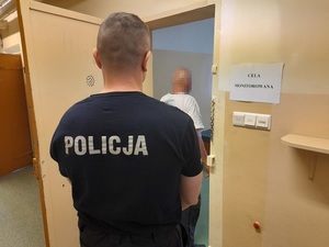 w otwartych drzwiach celi stoi zatrzymany mężczyzna. Za nim stoi policjant