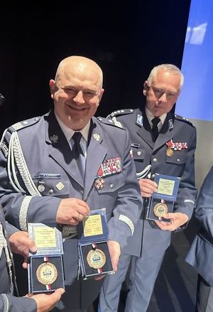 uśmiechnięty Komendant Wojewódzki Policji w Gdańsku w towarzystwie swojego zastępcy prezentuje pamiątkowy medal