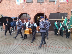 z kościoła wynoszona jest trumna. Z obu stron trumny maszerują policjanci z asysty honorowej