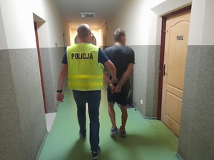 policjant prowadzi korytarzem mężczyznę skutego kajdankami