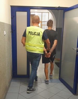 policjant przeprowadza przez drzwi mężczyznę skutego kajdankami