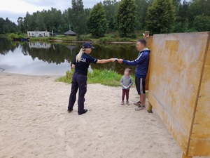 na jeziorem policjantka wręcza ulotkę mężczyźnie, przy którym stoi mała dziewczynka