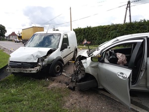 miejsce wypadku drogowego. Zderzone ze sobą dwa samochody: ford i toyota. Ford ma zniszczony przód, liczne wgniecenia karoserii i ubytki obudowy, uszkodzone koło. Toyota ma wgnieciony przód, koło od strony kierowcy ułożone jest poziomo. W aucie wystrzelona jest poduszka powietrzna od strony kierowcy. Dalej, za tymi pojazdami na jezdni znajduje się samochód ciężarowy