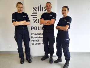 przy ścianie na tle roll up z napisem komenda powiatowa policji w Lęborku stoi troje młodych uśmiechniętych policjantów: dwie policjantki i policjant