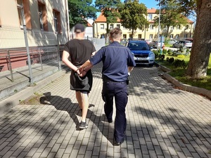 policjant prowadzi skutego kajdankami mężczyznę w kierunku radiowozu