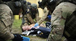 trzej policyjni kontrterroryści pochylają się nad leżącą na trawie osobą