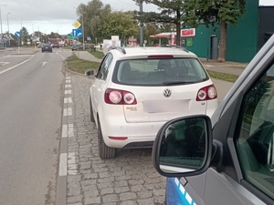 w mieście na poboczu drogi stoi biały vw golf. Za nim znajduje się policyjny radiowóz