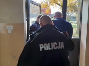 policjanci służby konwojowej wyprowadzają z budynku zatrzymanego mężczyznę