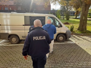 policjanci służby konwojowej prowadzą mężczyznę w kierunku nieoznakowanego radiowozu