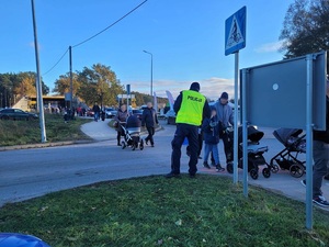 policjant w kamizelce odblaskowej przekazuje pieszemu element odblaskowy