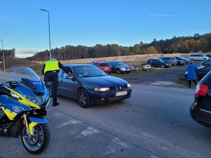 policjant w kamizelce odblaskowej przekazuje siedzącemu w samochodzie kierowcy apteczkę samochodową