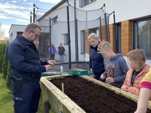 dwoje policjantów i dzieci sadzą do donicy cebulki kwiatów