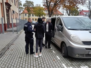 dwaj policjanci prowadzą do nieoznakowanego radiowozu kobietę i mężczyznę