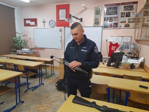 w sali uczelni policjant prezentuje pistolet maszynowy