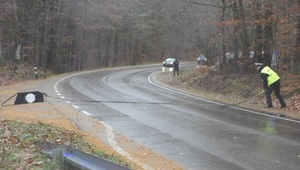 na jezdni policjant ruchu drogowego rozwinął policyjną kolczatkę. Jezdnią w jego kierunku jedzie samochód osobowy, za którym jedzie policyjny radiowóz z włączonymi sygnałami błyskowymi