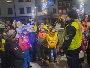 na placu policjantka ruchu drogowego mówi przez mikrofon do zgromadzonych wokół niej dzieci